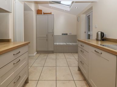 A kitchen with gray cabinets wooden countertops tiled floor bench with cushions and skylight at Castell in Abersoch