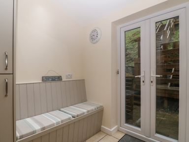 A small room with built in bench seating cushions a clock on the wall and double glass doors leading outside at Castell in Abersoch