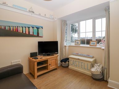 A living room with a television on a wooden cabinet a window seat with cushions and baskets near the window at Castell in Abersoch