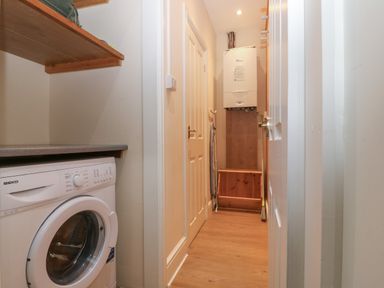 A narrow utility room with a washing machine a wooden shelf an ironing board and a boiler on the wall at Castell in Abersoch