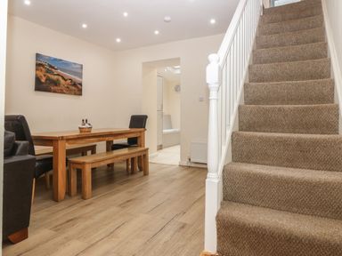 A dining area with a wooden table and bench and carpeted stairs beside it at Castell in Abersoch