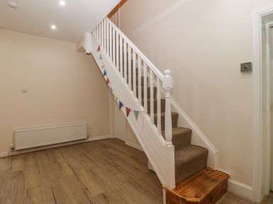 An empty hallway with wooden flooring a white staircase with carpeted steps a radiator on the wall and a door under the stairs at Castell in Abersoch