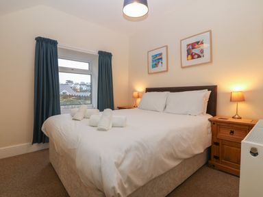 A bedroom with a bed with white linens and rolled towels two nightstands with lamps and a window with blue curtains at Castell in Abersoch