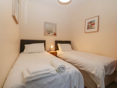 A bedroom with two single beds a bedside table with a lamp and framed pictures on the walls at Castell in Abersoch