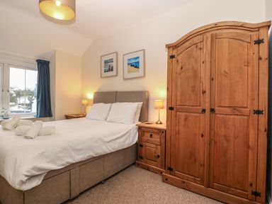 A bedroom with a double bed bedside tables wooden wardrobe and window with blue curtains at Castell in Abersoch