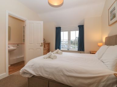A bedroom with a bed and rolled towels a window with blue curtains and an open door leading to a bathroom at Castell in Abersoch