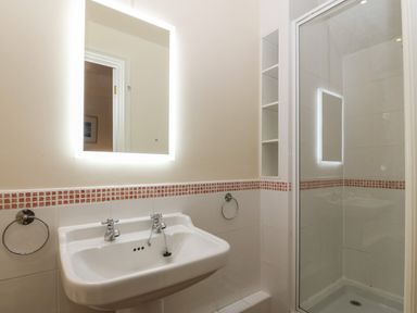 A bathroom with a sink, illuminated mirror, towel rings, and a shower cubicle at Castell in Abersoch