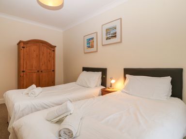A bedroom with two single beds with white bedding a wooden wardrobe and framed pictures on the wall at Castell in Abersoch