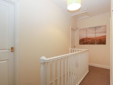 A hallway with white railings doors and a three-panel wall art at Castell in Abersoch