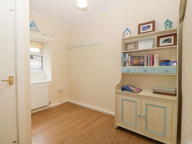 A small room with wooden flooring a window a white cabinet with books and pictures and a door at Castell in Abersoch