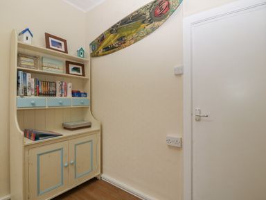 A corner with a cream and blue wooden cabinet with books and framed pictures on shelves and a decorative surfboard on the wall at Castell in Abersoch