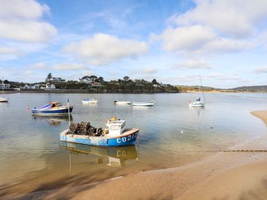 Several boats on calm water near a sandy shore with houses and trees in the background at Castell in Abersoch