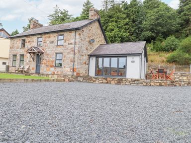 A stone cottage with a slate roof and gravel driveway with outdoor chairs and table at The Cottage in Llaniestyn