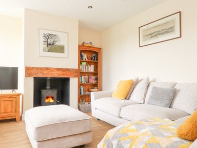 A living room with a beige sofa and ottoman a wood stove fireplace a wooden bookshelf and a television at The Cottage in Llaniestyn