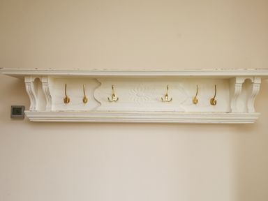 A wall mounted wooden coat rack with six gold hooks and decorative detailing at The Cottage in Llaniestyn