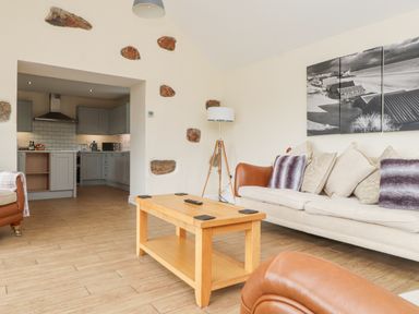A living room with a beige sofa with cushions a wooden coffee table a floor lamp and an open kitchen at The Cottage in Llaniestyn