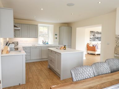 A kitchen with grey cabinets an island and wooden floor next to a dining table and chairs at The Cottage in Llaniestyn
