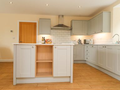 A kitchen with gray cabinets a wooden floor a central island and appliances at The Cottage in Llaniestyn