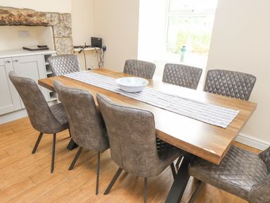 A dining room with a wooden table and eight grey upholstered chairs at The Cottage in Llaniestyn