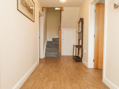 A hallway with wooden floor and carpeted stairs with a coat rack and framed picture on the wall at The Cottage in Llaniestyn