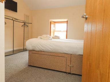 A bedroom with a bed and towels on it a wooden window hangers and a television on the wall at The Cottage in Llaniestyn
