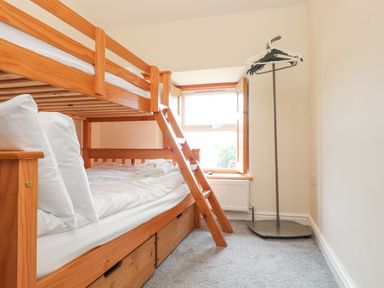 A bedroom with a wooden bunk bed and a clothes rack near a window at The Cottage in Llaniestyn