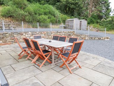 An outdoor patio with a rectangular wooden table surrounded by eight chairs with black seats and backs at The Cottage in Llaniestyn
