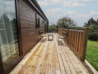 An outdoor wooden deck with chairs and a table at Castell Chalet Penrhos near Pwllheli