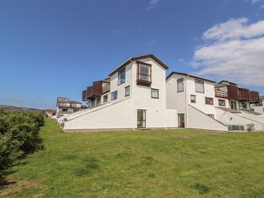 A row of white multi-story buildings with sloped walls and balconies overlooking a grassy lawn at Sunset Sands in Deganwy