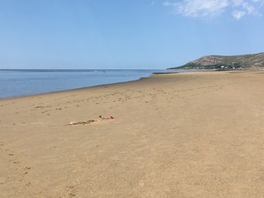 A wide sandy beach with calm water and a hill in the distance at Sunset Sands in Deganwy