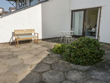 An outdoor patio with a wooden bench and a metal table with two chairs near sliding glass doors at Sunset Sands in Deganwy
