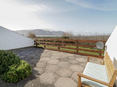 A patio with hexagonal stone tiles a wooden bench with cushion and a wooden fence overlooking mountains at Sunset Sands in Deganwy
