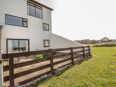 A fenced patio area next to a white house with multiple windows and a glass door at Sunset Sands in Deganwy