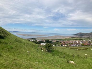 A coastal village with houses near the shore and hills with grass in the foreground at Sunset Sands in Deganwy