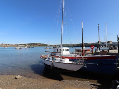 Sailboats and motorboats moored by a dock near a waterfront with hills in the background at Sunset Sands in Deganwy