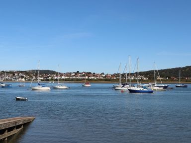 A body of water with multiple sailboats moored and houses visible in the background at Sunset Sands in Deganwy