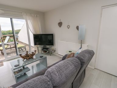 A living room with a grey sofa a glass coffee table a television and sliding glass doors leading to an outdoor patio at Sunset Sands in Deganwy