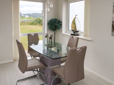 A dining area with a glass table and four chairs beside windows and a decorative plant at Sunset Sands in Deganwy