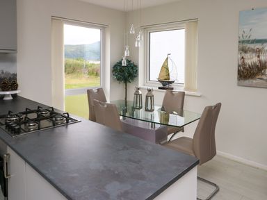 A kitchen with a gas stove island and a dining table with chairs near windows at Sunset Sands in Deganwy