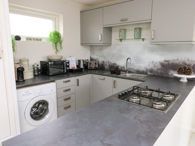 A kitchen with grey cabinets black countertop a gas stove washing machine and window at Sunset Sands in Deganwy