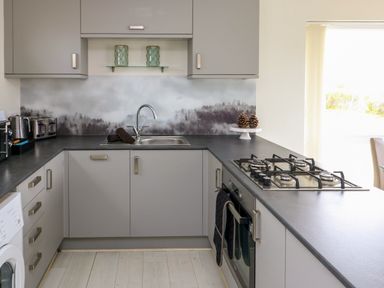 A kitchen with grey cabinets a gas stove a sink and a window at Sunset Sands in Deganwy
