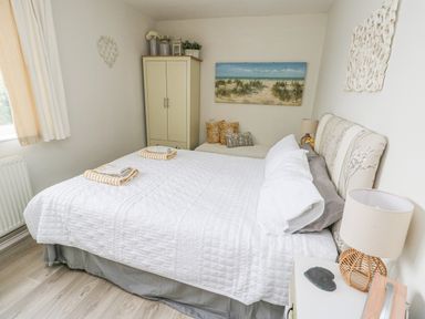 A bedroom with a bed covered by white quilt and towels on top bedside tables with lamps and a wardrobe near a window at Sunset Sands in Deganwy