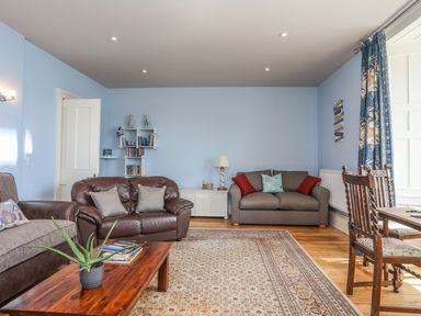 A living room with sofas a wooden coffee table a carpet a dining table and chairs at Gadlys House - Waters Edge in Beaumaris