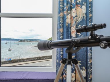 A telescope by a window with floral curtains overlooking boats on the water at Gadlys House - Waters Edge in Beaumaris