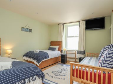 A bedroom with two single beds a wooden daybed a wall-mounted television and a window at Gadlys House Waters Edge in Beaumaris