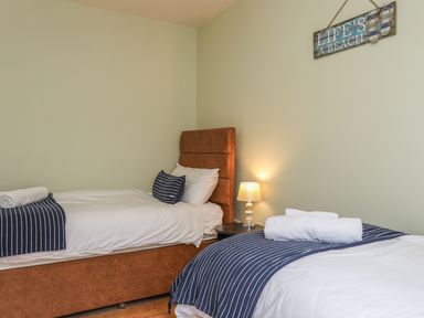 A bedroom with two single beds a bedside table with a lamp and a wall decoration at Gadlys House - Waters Edge in Beaumaris