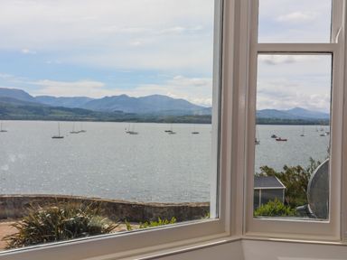 A window view overlooking a body of water with sailboats and distant mountains at Gadlys House - Waters Edge in Beaumaris