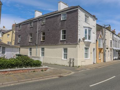 A street view of a three story building with a mix of brick and stucco walls and multiple windows in Beaumaris