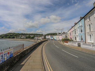 A coastal road with pastel-colored houses on one side and water on the other at Gadlys House Waters Edge in Beaumaris