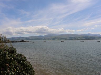 A body of water with boats, a pier, and mountains in the background at Gadlys House - Waters Edge in Beaumaris